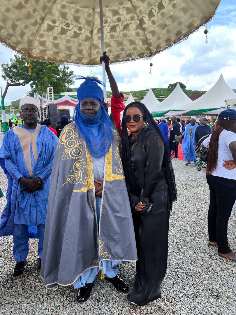 Anna Philemon Dara standing with a traditional ruler under a ceremonial parasol at an outdoor gathering.