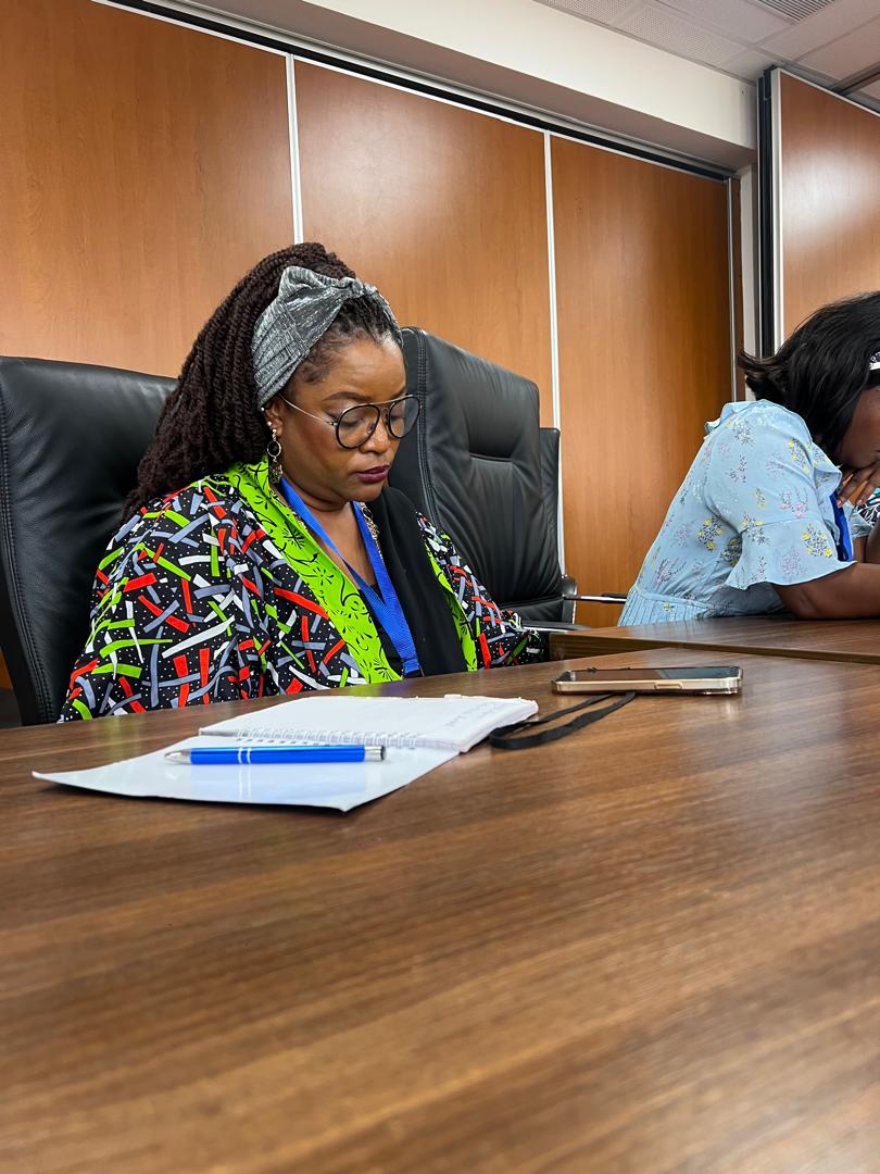 Anna Philemon Dara seated at a boardroom table taking handwritten notes during a working session.
