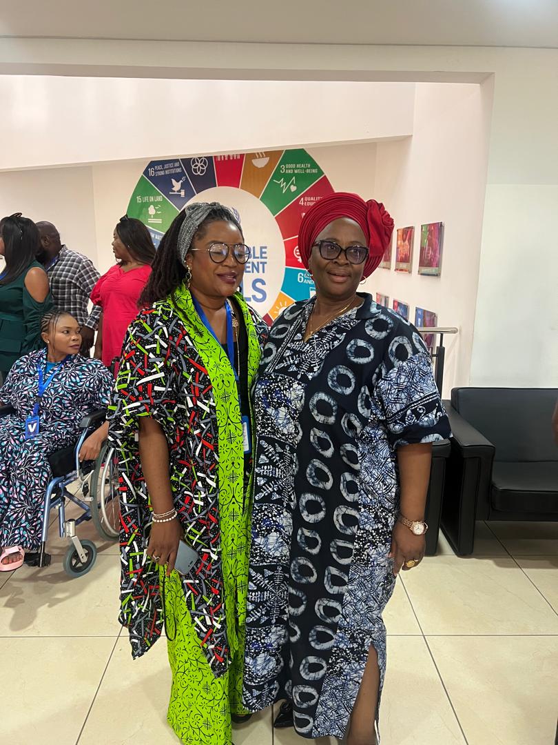 Anna Philemon Dara with a colleague in front of a Sustainable Development Goals wheel display.